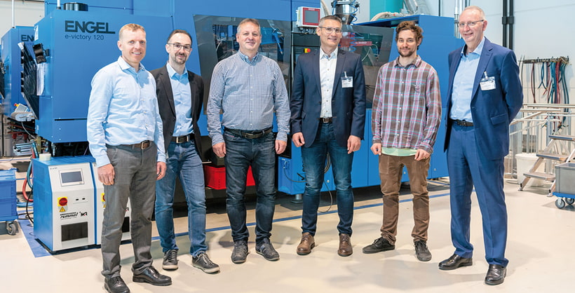 Image shows Hagleitner team members together with ENGEL employees in front of an injection moulding machine for simulation of plastic injection moulding
