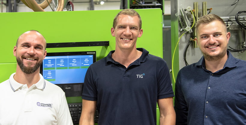 Bild zeigt Robert Jautz von KROSCHU, Alexander Ebner und David Kupfer von ENGEL vor einer grünen ENGEL Spritzgießmaschine und einem Terminal